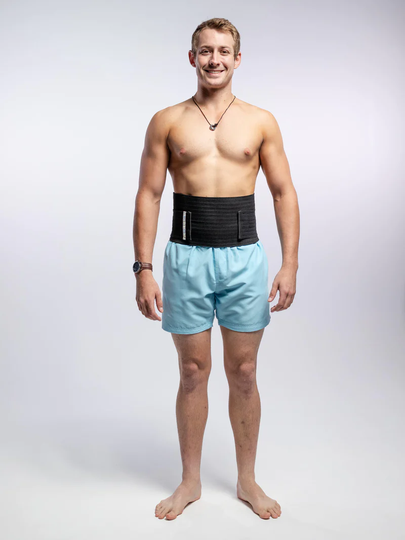 A man standing in a hernia support belt grey background