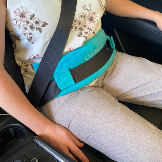 Woman wearing flowery shirt, sitting in car wearing blue Seat Belt Cushion to protect mid-riff from seat belt.